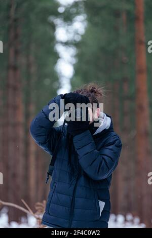 Unbekannter Mann, der in einem verschneiten Wald steht und eine Kamera hält Bis zu seinem Auge, das ein Foto in die Kamera schaut Stockfoto