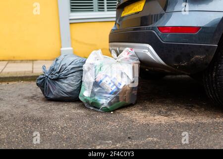 Woodbridge, Suffolk, UK März 01 2021: Plastiktüten voller Müll, die am Straßenrand hinter einem geparkten Auto zurückgelassen wurden Stockfoto