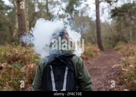 Ein unbekannter Mann, der von der Kamera weggeht, mit einer Wolke von Vape umringt sein Gesicht. Anti-Rauchen, Verdampfen, vape, Aufhören Rauchen Konzept Stockfoto