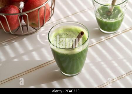Ein Glas grünen Saft mit einem Bambusstroh, mit Äpfeln im Hintergrund Stockfoto