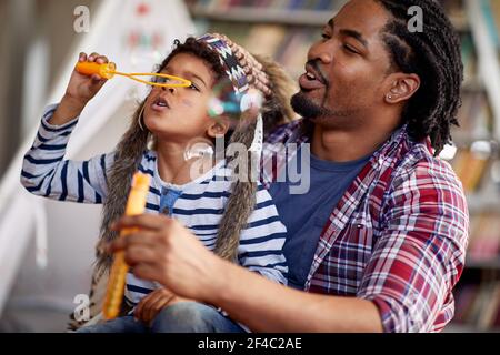 Ein kleiner Junge wie ein Inder gekleidet genießt Seifenblasen mit seinem Vater in spielerische Atmosphäre zu Hause. Familie, Zuhause, Freizeit Stockfoto