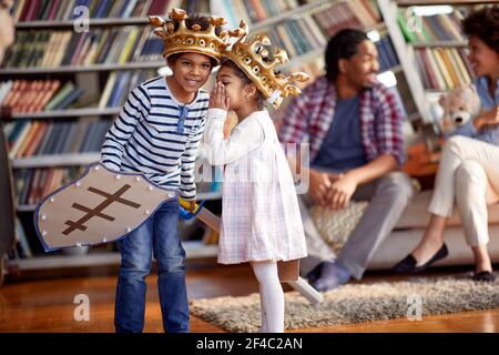 Kinder, die als Ritter gekleidet sind, flüstern und murmeln, während sie mit ihren Eltern in familiärer Atmosphäre zu Hause spielen. Familie, Zuhause, Freizeit Stockfoto