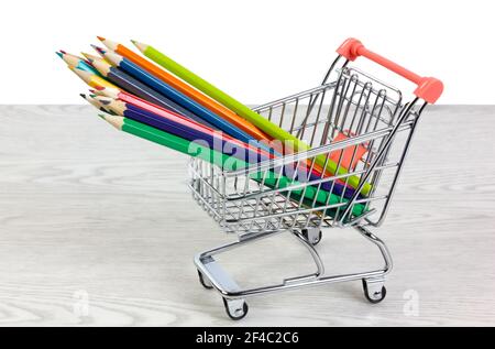 Buntstifte in einem Miniatur-Einkaufswagen auf einem weißen Holztisch auf weißem Hintergrund Stockfoto