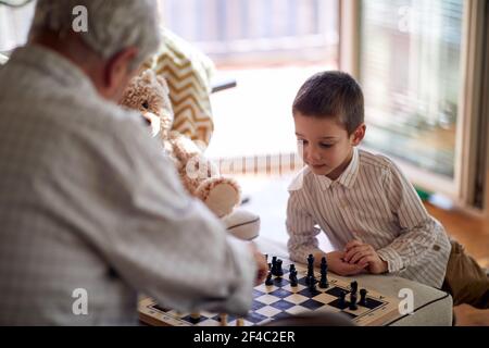 Ein kleiner Enkel spielt gerne ein Schachspiel mit seinem Opa in einer entspannten Atmosphäre zu Hause. Familie, Zuhause, Freizeit Stockfoto