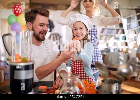 Ein kleines Mädchen und ihr Vater posieren für ein Foto, während sie ein Essen in einer fröhlichen Atmosphäre zu Hause zusammen vorbereiten. Familie, Haus, Küche Stockfoto