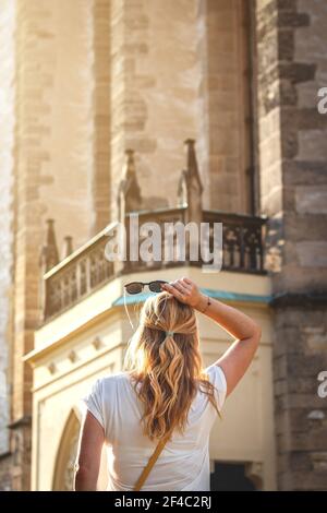 Blonde Frau mit Sonnenbrille in der Altstadt. Junge Frau hält Sonnenbrille in der Hand und schaut zur Kirche Stockfoto