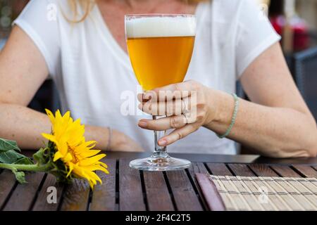 Frau sitzt im Restaurant im Freien und trinkt Bier, Stadtleben im Sommer. Nahaufnahme der weiblichen Hand mit einem Glas Bier vom Fass Stockfoto