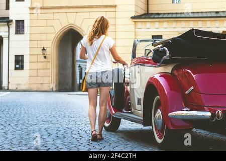 Junge Frau und Retro-Oldtimer in der Altstadt. Frau öffnet die Tür eines Retro-Autos und verlassen Stadt für einen Urlaub. Stockfoto