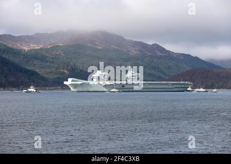 Cove, Argyle und Bute, Schottland, Großbritannien. März 2021, 20th. IM BILD: Die Leute schauen, wie die HMS Queen Elizabeth nach fast einer Woche in Loch Long in Glenmallan, wo sie Treibstoff, Munition und andere Vorräte annahm, vor den Marineübungen, die Teil der britischen Carrier Strike Group 2021 sind, die Segel setzte. Quelle: Colin Fisher/Alamy Live News Stockfoto