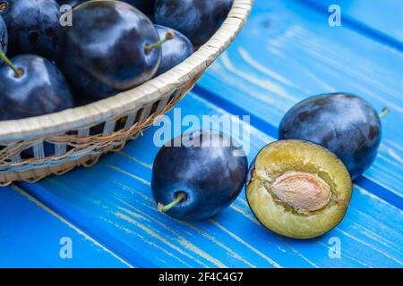 Pflaumen auf blauem Holztisch. Frisch geerntete reife Früchte. Nahaufnahme der halbierten Pflaume Stockfoto