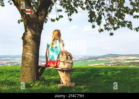 Tourist Frau sitzt auf Bank unter Kirschbaum während der Wanderung. Blick auf die Landschaft. Wandern Rucksacktouristen Entspannung. Stockfoto