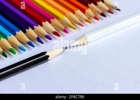 Weiße und schwarze Stifte fordern sich gegenseitig heraus. Viele Buntstifte liegen in einer Reihe. Stockfoto