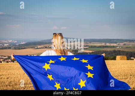 Frau mit winkender EU-Flagge auf dem Land. EU-Flagge in weiblichen Händen. Stockfoto
