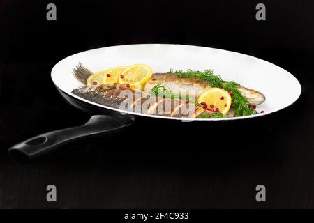 Zwei ganze Seebarsch Kochen in der Pfanne mit Dill, Zitrone Und rosa Pfefferkörner Stockfoto