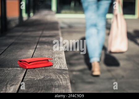 Frau verlässt eine Bank, wo sie ihre Ledertasche vergessen hat. Geldbörse auf der Stadtstraße verloren Stockfoto