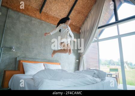 Attraktive asiatische Frau, die morgens auf dem Bett sprang, am Morgen, fühlte sie sich sehr erfrischt, natürliches Fensterlicht. Stockfoto