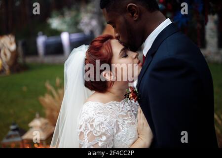 Portrait von schönen Paar auf Hochzeitszeremonie, schöner afroamerikanischer Mann mit entzückenden weißen Frau kuscheln in der Nähe dekorierten Bogen, genießen Sie glücklich Stockfoto