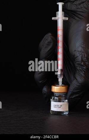Hand in schwarzen Gummihandschuhen hält Glasfläschchen mit Impfstoff. Nahaufnahme. Stockfoto