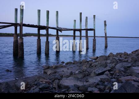 Der baufällige herunterfallende alte Fischerboot-Kai, der bereit für den Abriss ist, bei Morgendämmerung bei Ebbe zeigt die faulen Hölzer und Masten. Stockfoto