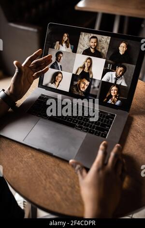 Der junge afroamerikanische Geschäftsmann schaut in den Laptop-Bildschirm, spricht per Videokommunikation mit seinen Kollegen. Unternehmer, sitzen in Stockfoto