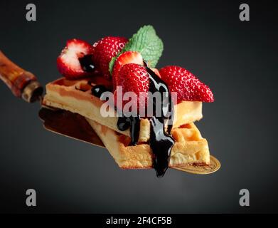 Belgische Waffeln mit Erdbeeren, Minze und Schokolade Soße auf schwarzem Hintergrund. Stockfoto