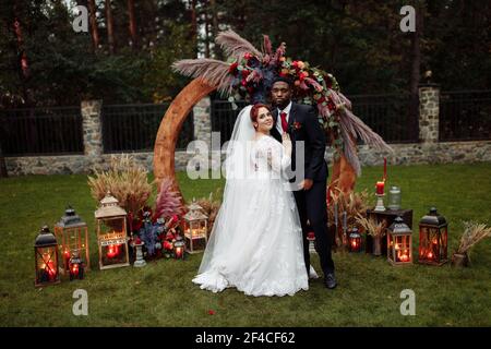 Schönes Paar auf Hochzeitszeremonie, schöner afroamerikanischer Mann mit entzückenden weißen Frau stehen in der Nähe dekorierten Bogen, kuscheln, genießen glücklich Stockfoto