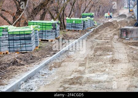 Stapel von Pflastersteinen auf einer Baustelle entlang eines vorbereiteten Pflasterweges in einer Frühlingsstadt Straße. Stockfoto