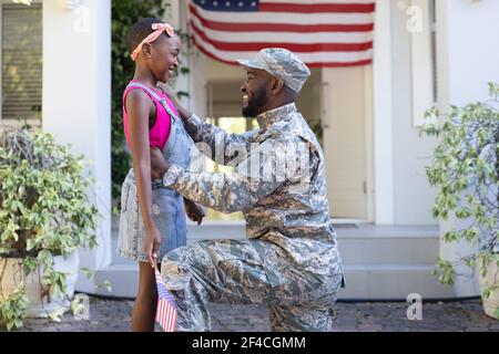 afroamerikanische männliche Soldat Vater Gruß lächelnd Tochter hält Flagge Vor dem Haus Stockfoto