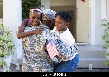 Rückansicht des afroamerikanischen Soldaten Vater umarmt Sohn und Tochter vor dem Haus Stockfoto