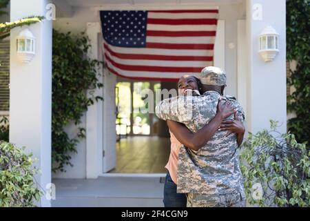 African american männlich Soldat umarmt lächelnde Frau vor amerikanische Flagge vor dem Haus Stockfoto