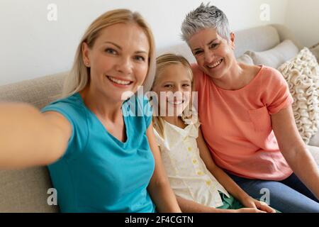 Kaukasische Mutter sitzt auf der Couch und nimmt Selfie mit lächelnder Tochter Und Großmutter Stockfoto