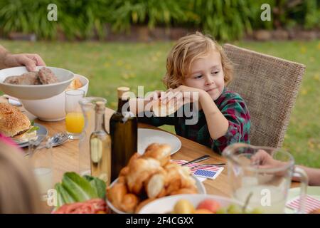 Lächelnder kaukasischer Junge hält Hamburger essen mit Familie in Garten Stockfoto