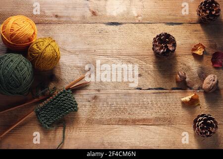 Ein Stück Stricken mit Holznadeln und Garn zwischen Blättern und Tannenzapfen, Herbst Stricken. Stockfoto