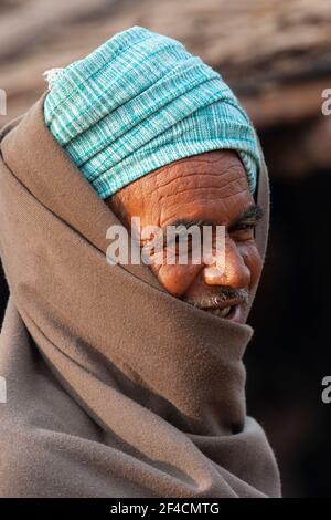 Lächelnder Mann aus Indien mit hellblauem Kopftuch und braunem Schal. Er hat ein frech Grinsen und ein ansteckendes Lächeln. Stockfoto