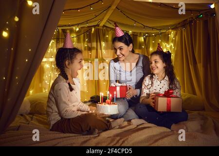 Die Familie feiert den Geburtstag eines Kindes, das in einem Zeltbett mit gelben LED-Lampen sitzt. Stockfoto