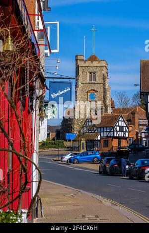 Pinner Village High Street mit Carluccios Restaurant & Starbucks auf der linken Seite & Saint John the Baptist, mittelalterliche Kirche auf einem Hügel im Hintergrund. Stockfoto