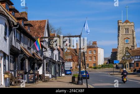 Pinner Village High Street. Historisches Queen's Head Pub & Pizza Express auf der linken Seite & Saint John the Baptist, mittelalterliche Kirche auf einem Hügel im Hintergrund. Stockfoto