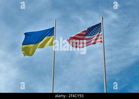 Flaggen der Ukraine und USA - Vereinigte Staaten von Amerika Winken im Wind an Polen auf bewölktem Himmel Hintergrund Stockfoto