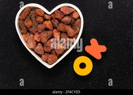 Haufen getrockneter Erdbeeren in einer herzförmigen Schüssel mit Holzblock Buchstaben Schreibweise okay. Gesundes Snack-Konzept. Stockfoto