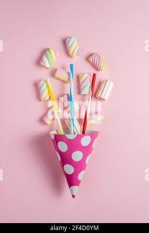 Bunte Marshmallows mit Party Hut auf rosa Hintergrund. Kreatives, minimalistisches Urlaubskonzept. Stockfoto