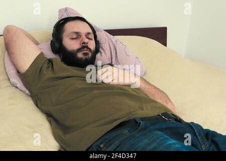 Nahaufnahme eines kaukasischen Bartmannes, der lügt Im Bett und Musik über Kopfhörer hören Stockfoto