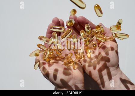 Fischöl Kapseln Set. Omega-Säuren. Nahrungsergänzungsmittel. Omega-3 Fettsäuren.Fischöl Gelatine Kapseln Levitation über männliche Hände auf einem weißen Stockfoto