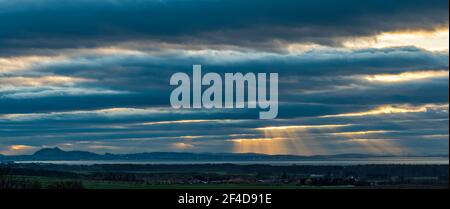 East Lothian, Schottland, Großbritannien, 20th. März 2021. UK Wetter: Sonnenuntergang am Frühlings-Tagundnachtgleiche. Ein wolkenverhallter Himmel über dem markanten Umriss von Edinburgh und Arthur's Sitz ermöglicht einen Ausbruch von Sonnenstrahlen durch, wie die Sonne untergeht Stockfoto