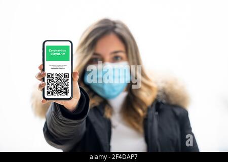 Defocused junges Mädchen trägt eine Gesichtsmaske hält ein Smartphone mit einem Beispiel von Covid-19 Immunität Pass. Stockfoto