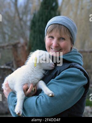 Roskow, Deutschland. März 2021, 15th. Die Bäuerin Katja Behling vom Skuddenhof in Weseram hält Danika, ein Lamm, das am 7. März 2021 geboren wurde, in den Armen. Zusammen mit ihrem Mann betreibt die gelernte Handelsverkäuferin die Zucht von Skudden auf dem Hof, der kleinsten einheimischen Schafrasse, die zu den ältesten Hausschafrassen gehört und weiße Mischwolle produziert. Die Skudde ist auf der Roten Liste der gefährdeten Tierrassen. Quelle: Soeren Stache/dpa-Zentralbild/ZB/dpa/Alamy Live News Stockfoto