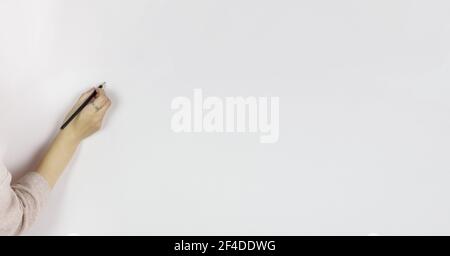 Weibliche Hand hält Bleistift auf weißem Hintergrund, schreibt in Bleistift auf einer grauen Wand, Copy Space. Grauer Hintergrund. Hand mit Stift an grauer Wand. Stockfoto