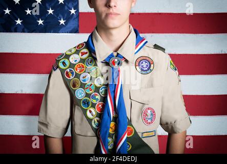 Porträt eines jungen Pfadfinderbuben, der vor der Tür steht Eine amerikanische Flagge Stockfoto