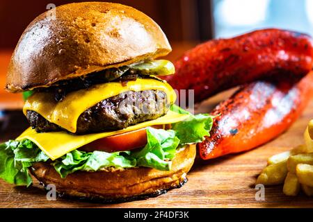 Nahaufnahme eines Cheeseburgers mit Tomaten, Gurken und Salat, serviert mit Pommes Frites und gerösteten roten Paprika Stockfoto