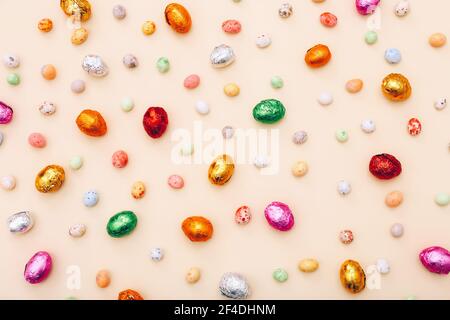 Osterschokolade Mini-Eier in einer bunten Folie eingewickelt, auf einem beigen Hintergrund verstreut Stockfoto