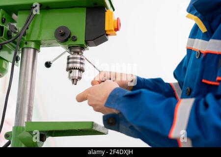 Ein junger Mann aus nächster Nähe, der eine Bohrmaschine in der Fabrik benutzt Stockfoto